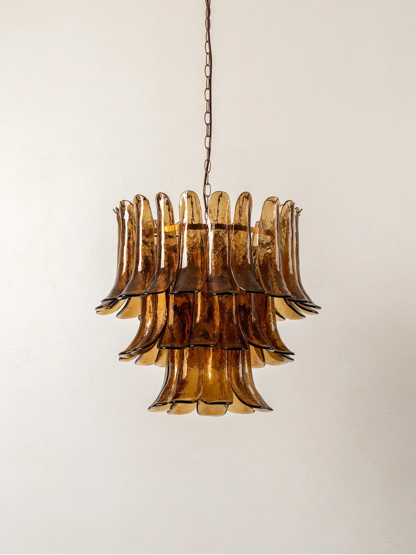 A mid-century modern tiered chandelier with a fluted amber glass shade and a dark metal chain, shown hanging against a plain off-white wall.