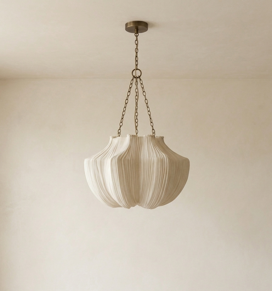 A modern pendant light with a pleated, textured shade in a warm off-white or cream color, suspended by a bronze-toned chain from a matching ceiling canopy against a neutral cream wall.