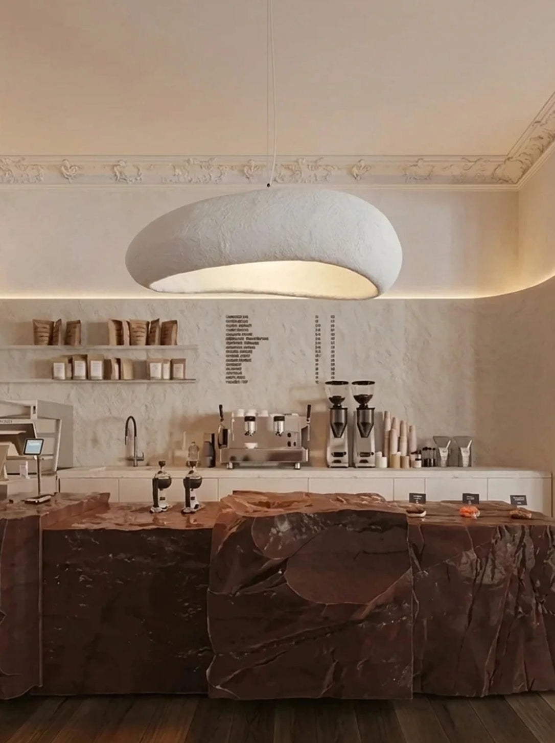 A modern interior scene with a large white dome pendant light hanging over a dark brown marble island in a warm, minimalist kitchen or bar space.