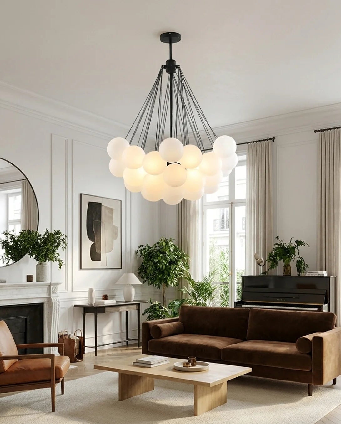 A modern multi-light pendant chandelier with a cloud of glowing frosted glass globes hangs in a bright, contemporary living room with a brown leather sofa, wooden coffee table, and beige rug.