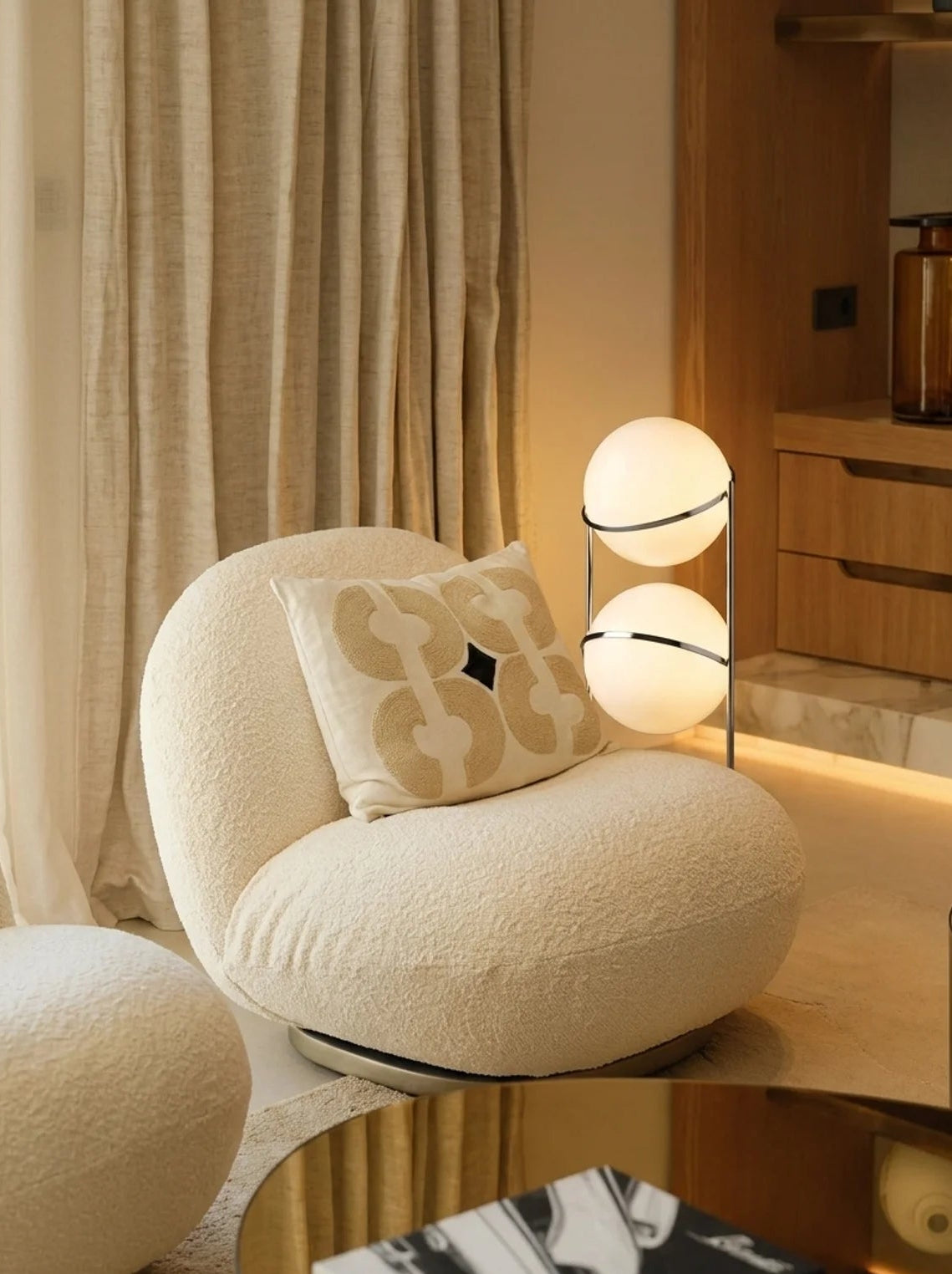 A modern round upholstered accent chair in a warm cream bouclé fabric, styled with a matching patterned throw pillow in a contemporary living room setting.