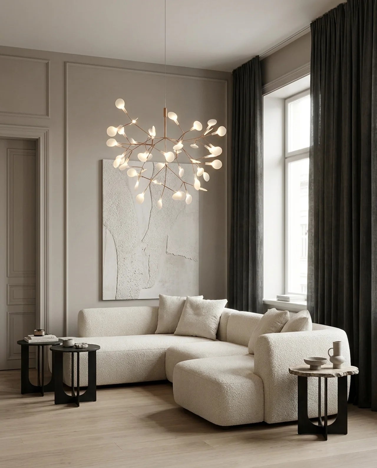 A modern living room featuring a large cream boucle sectional sofa with a chaise, styled with black side tables, a decorative wall art piece, and a unique branch-like chandelier hanging from the ceiling.