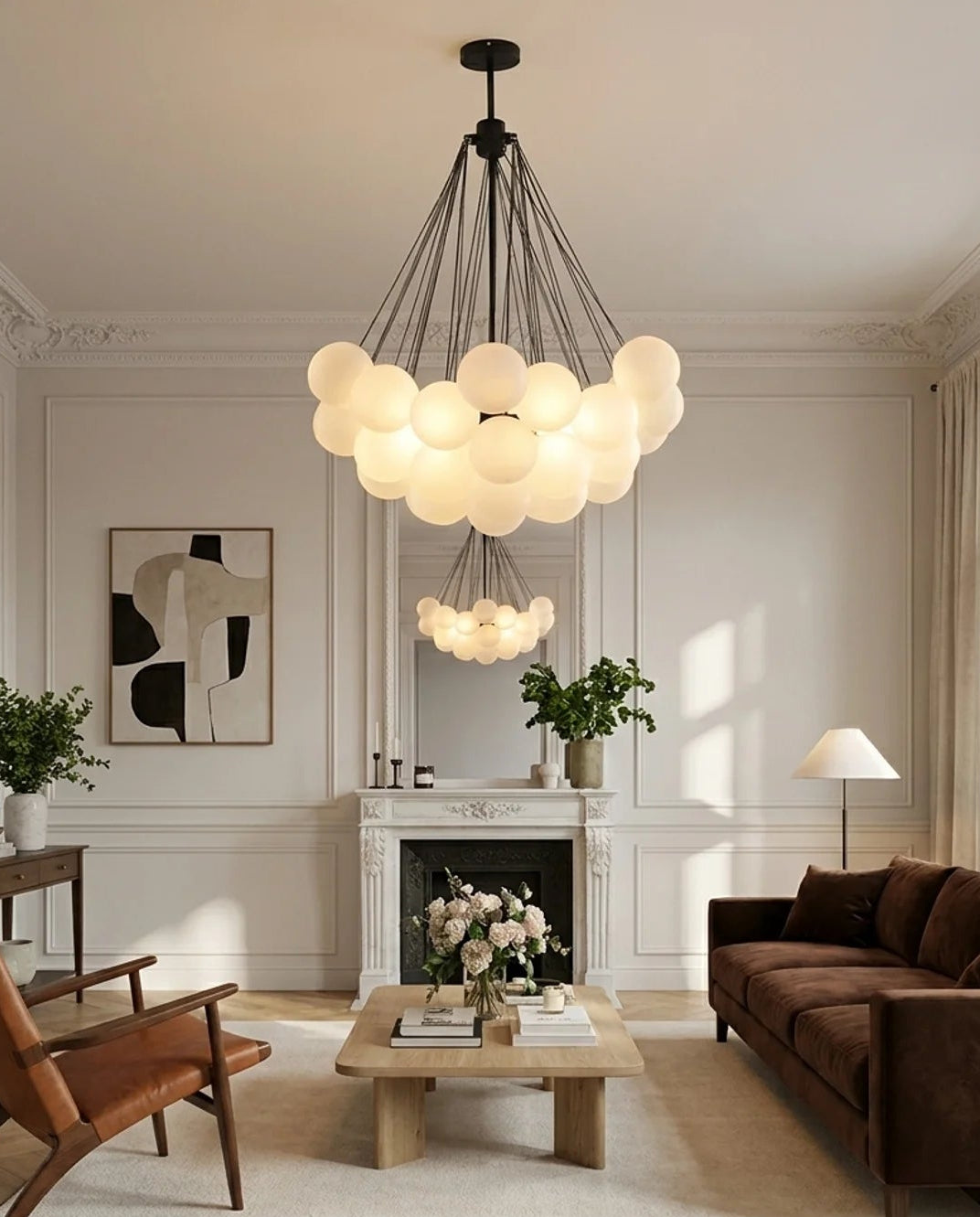 A modern multi-light pendant chandelier with glowing frosted glass globe bulbs hangs in a bright, elegant living room with a brown sofa, wooden coffee table, and fireplace.